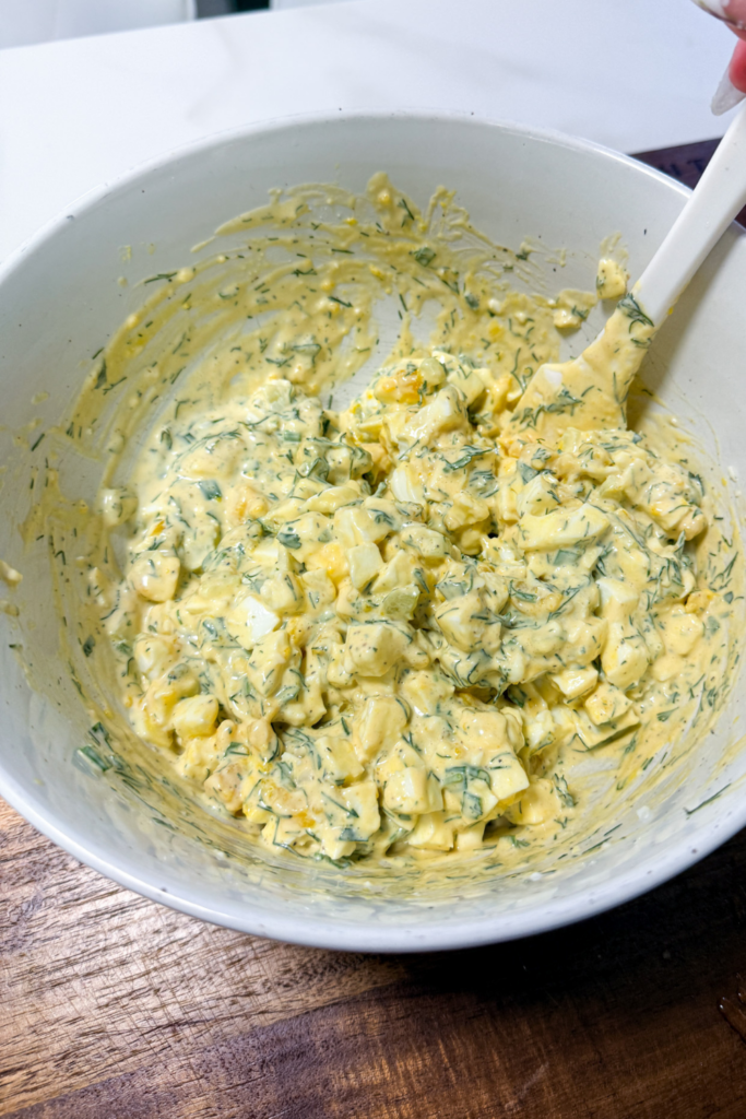 Finished creamy egg salad with dill and celery in mixing bowl