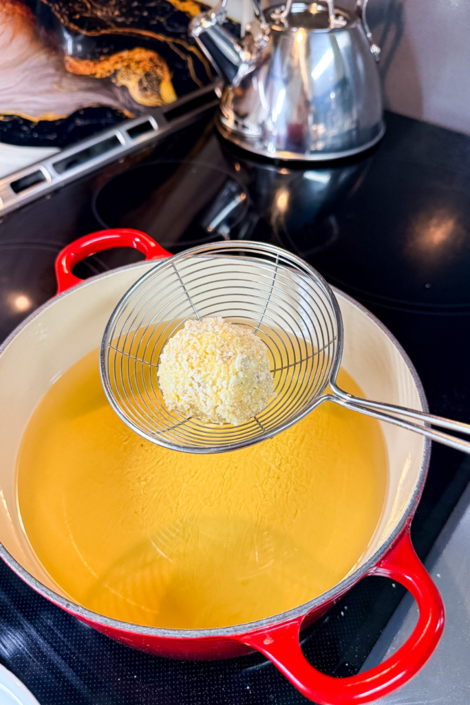 Lowering breaded croquette into hot oil using a spider strainer
