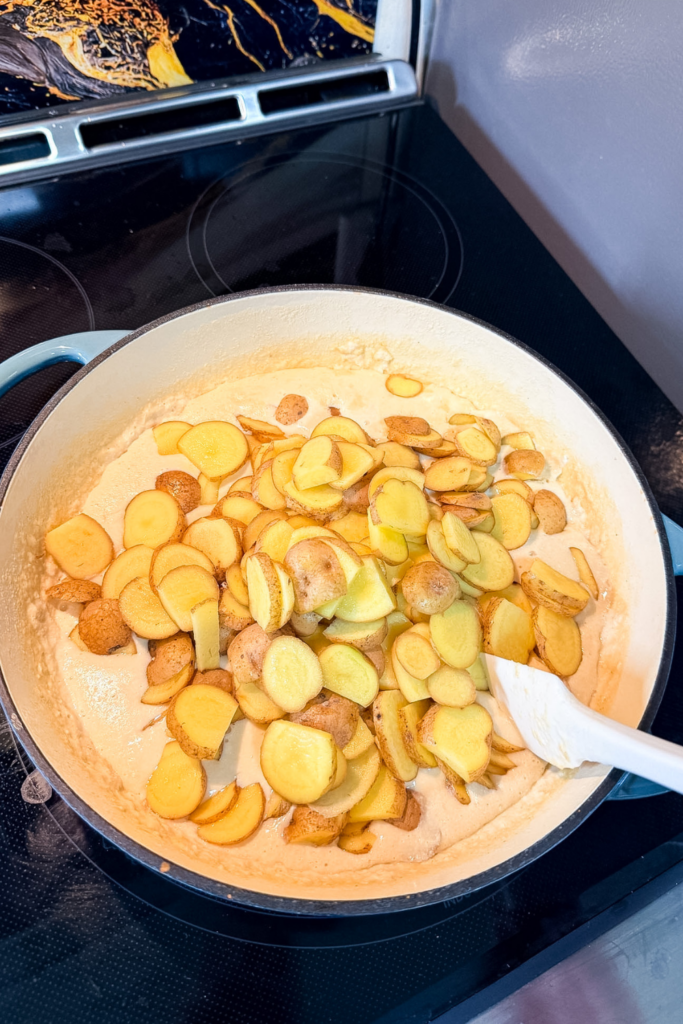 adding sliced Yukon gold potatoes to creamy gratin sauce in cast iron pan