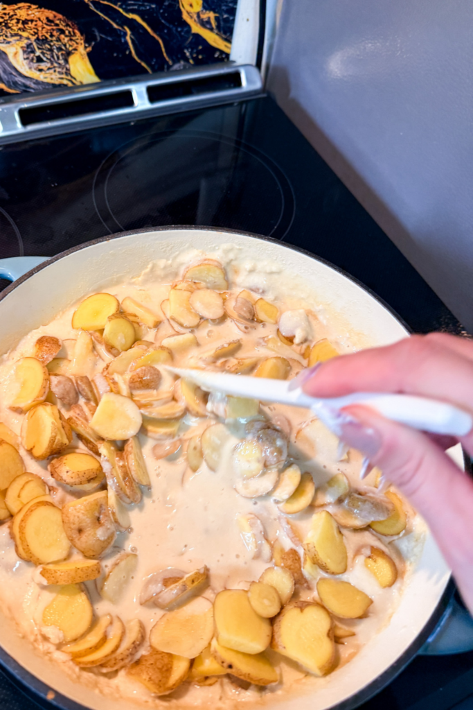 stirring sliced potatoes in creamy sauce while making potatoes au gratin