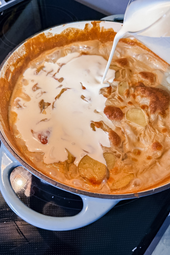 pouring warm heavy cream over baked potato gratin