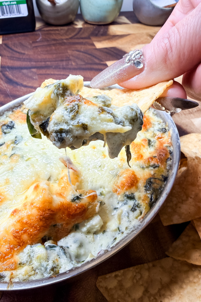 Creamy spinach artichoke dip scooped onto a tortilla chip showing melted cheese stretch.