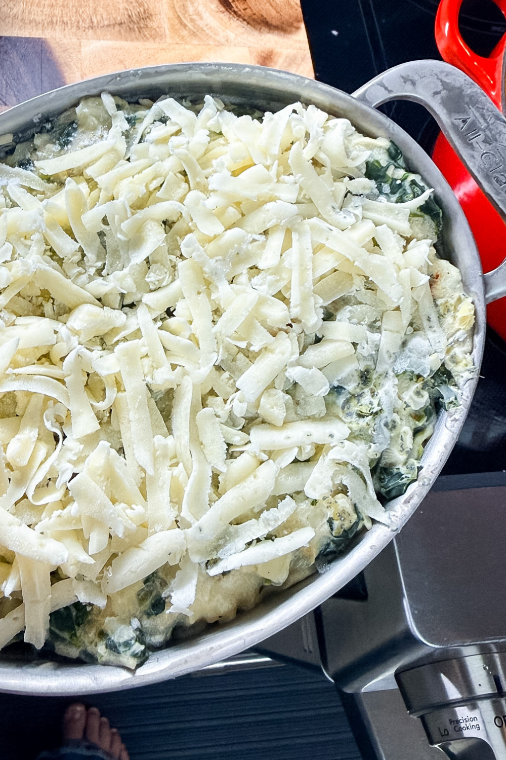 Frozen spinach artichoke dip in a small casserole dish topped with shredded cheese before baking.