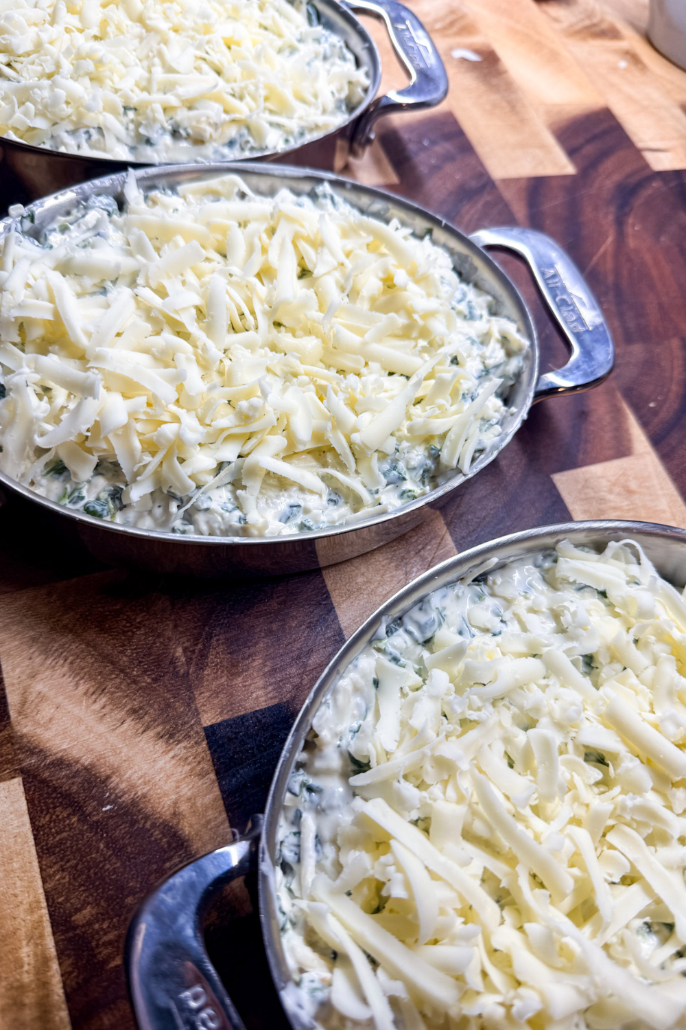Unbaked spinach artichoke dip topped with shredded cheese in small casserole dishes ready for the oven.