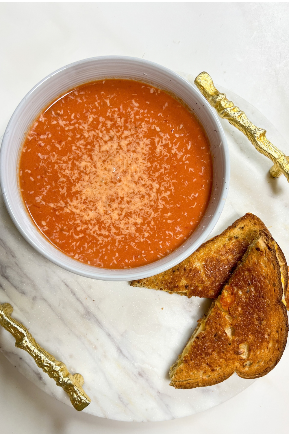 Overhead view of creamy tomato soup with grilled cheese on marble serving board