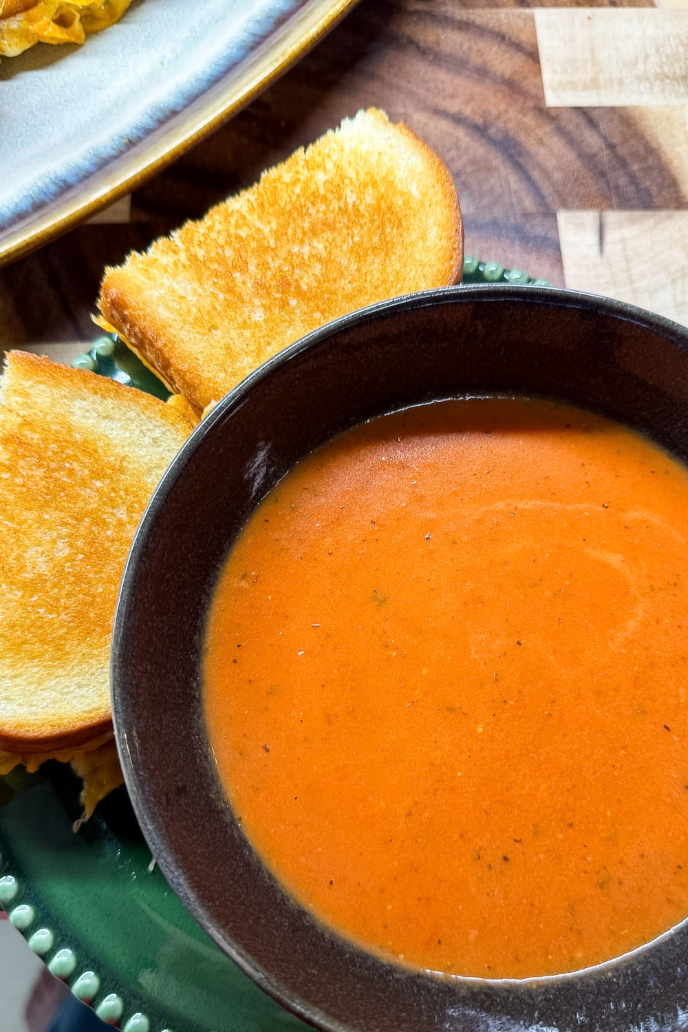 Creamy tomato soup served with toasted grilled cheese sandwiches on plate