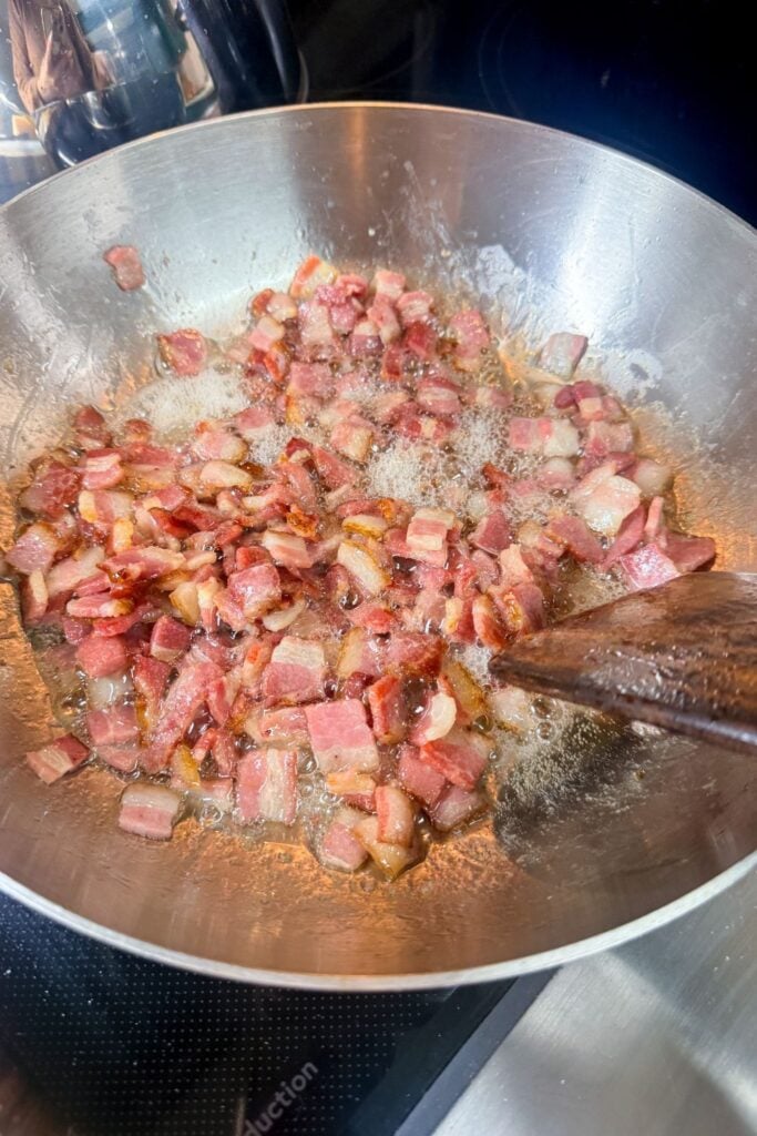 Diced bacon cooking in skillet with fat rendering for carbonara
