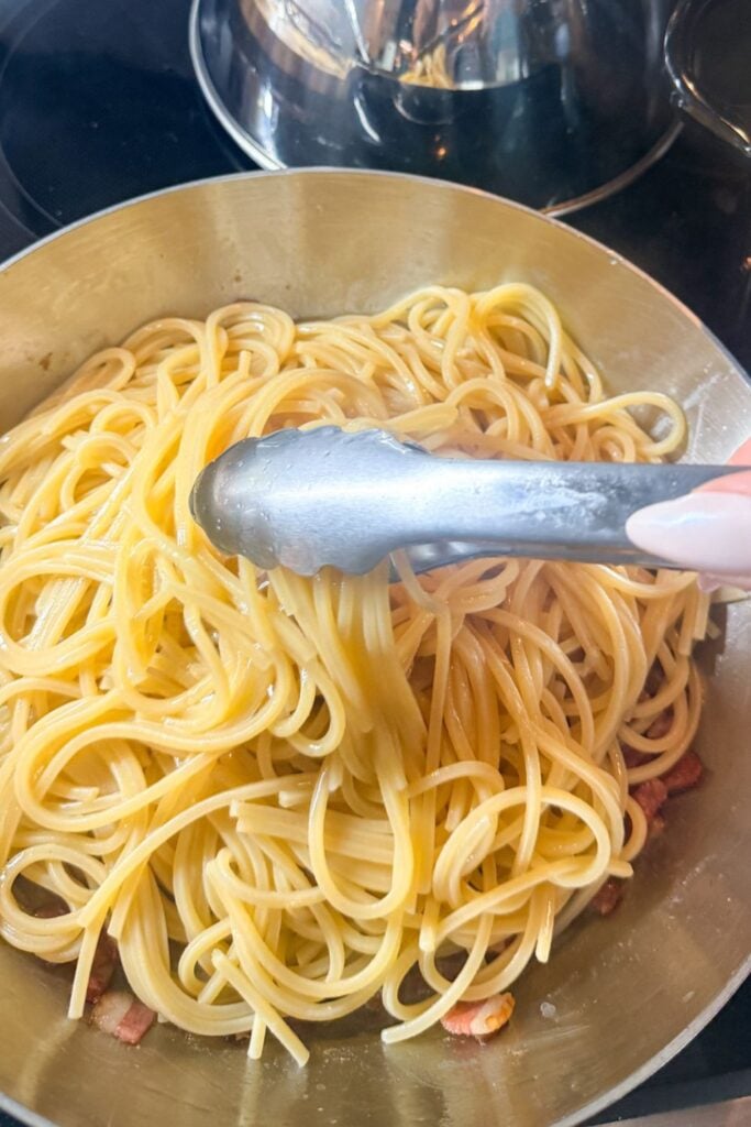 Cooked spaghetti added to skillet with bacon for carbonara