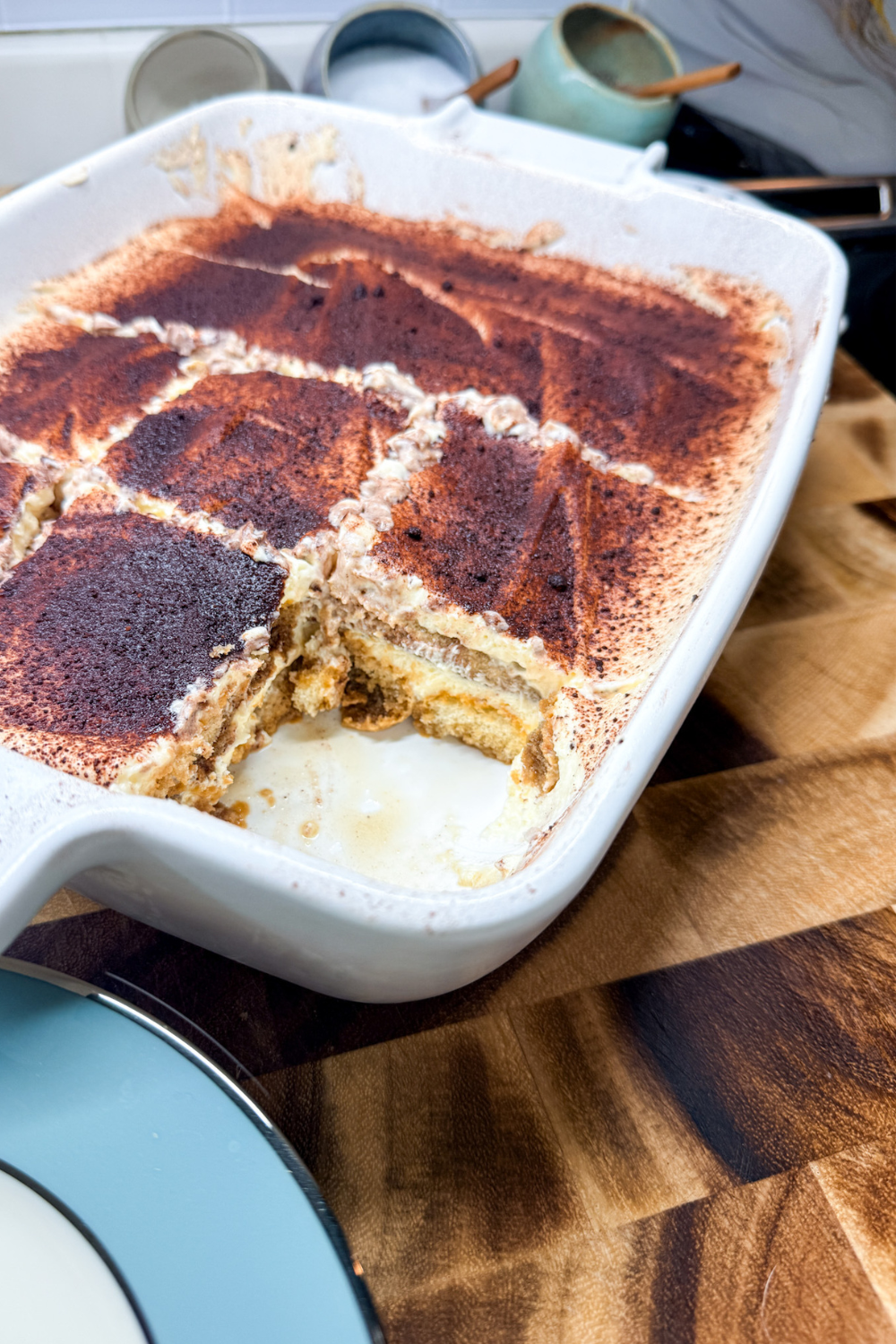 Homemade tiramisu in a baking dish with cocoa powder topping and a slice removed showing creamy layers