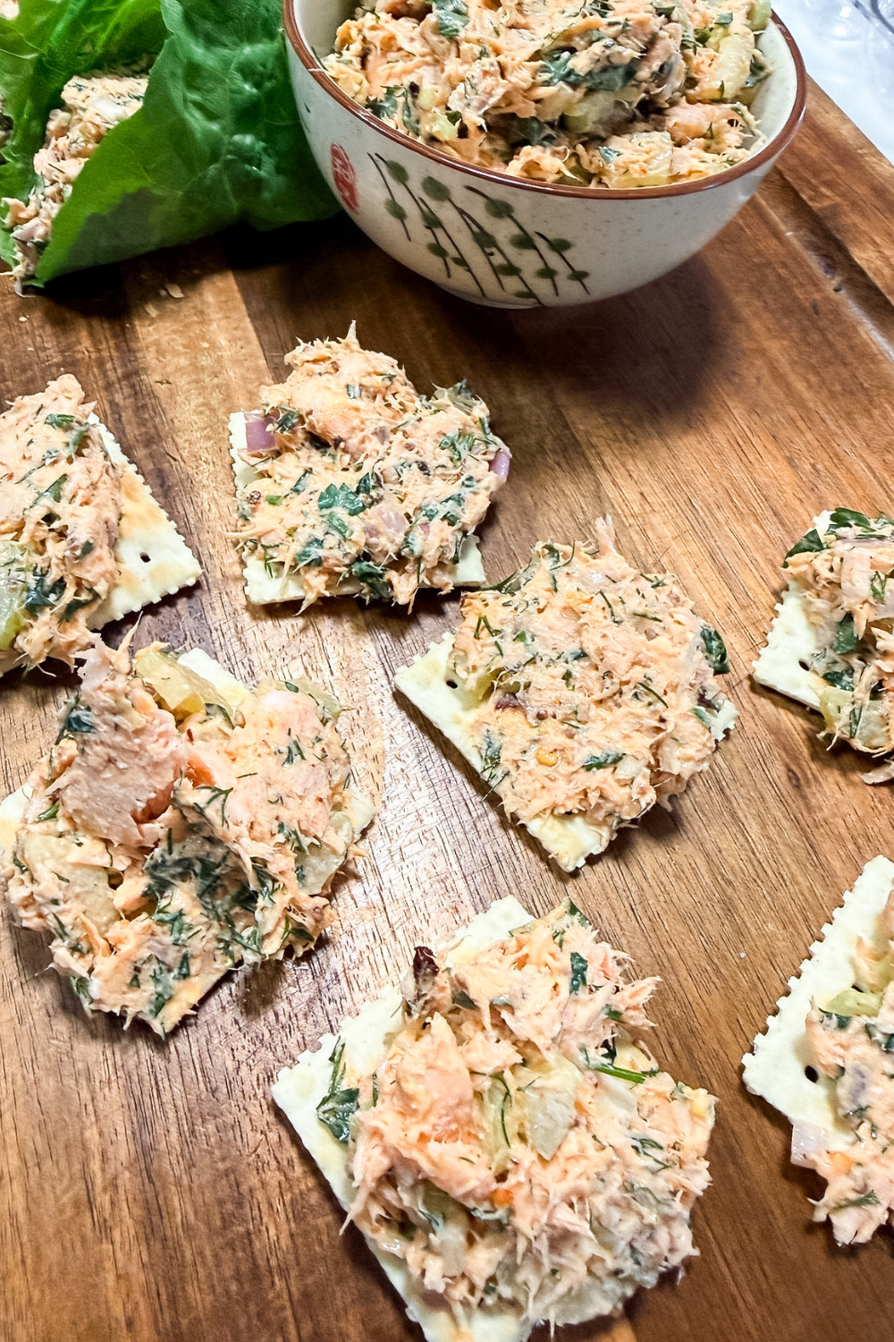 Salmon salad served with crackers and lettuce wraps on a wooden board