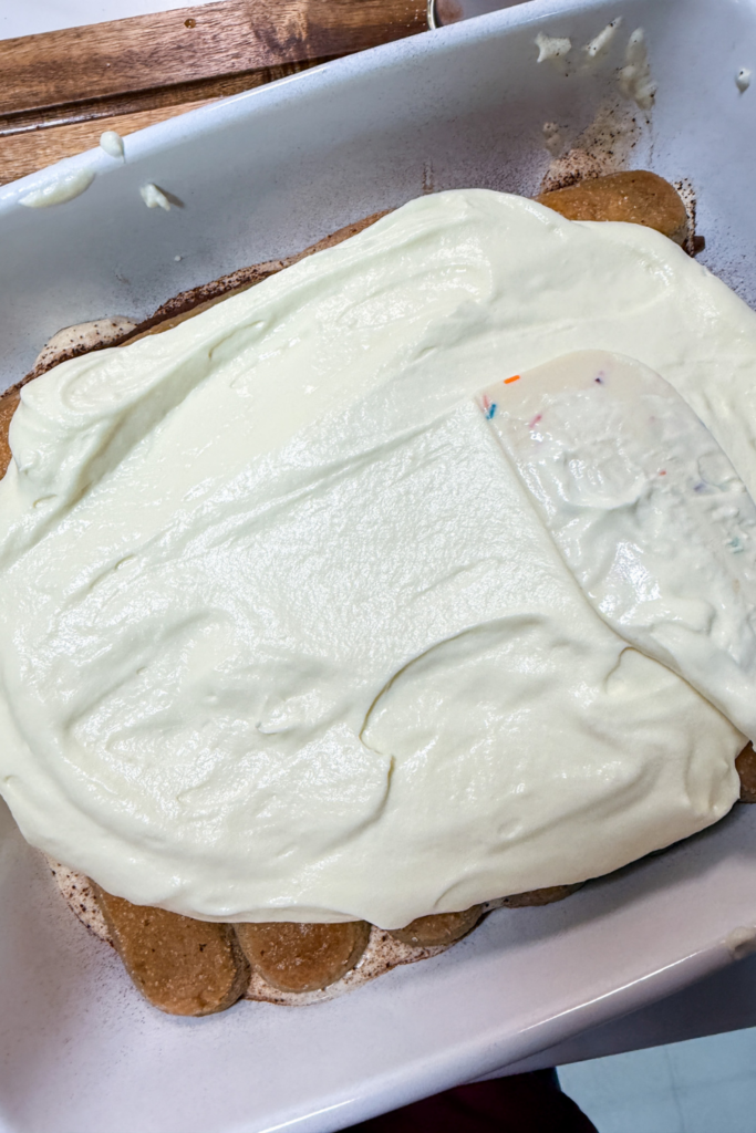 Spreading mascarpone cream over ladyfingers while assembling tiramisu
