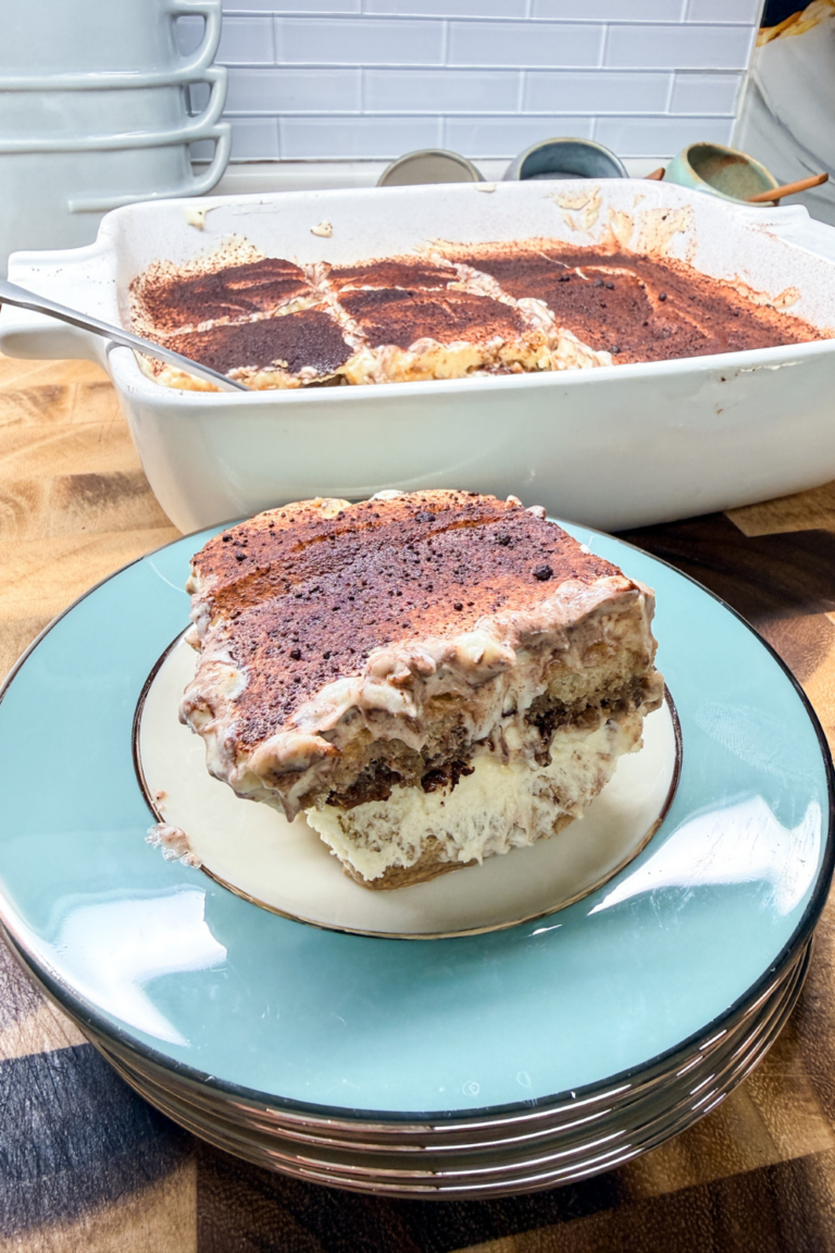 Easy homemade tiramisu recipe in a baking dish with a plated slice, layered with mascarpone cream and cocoa powder