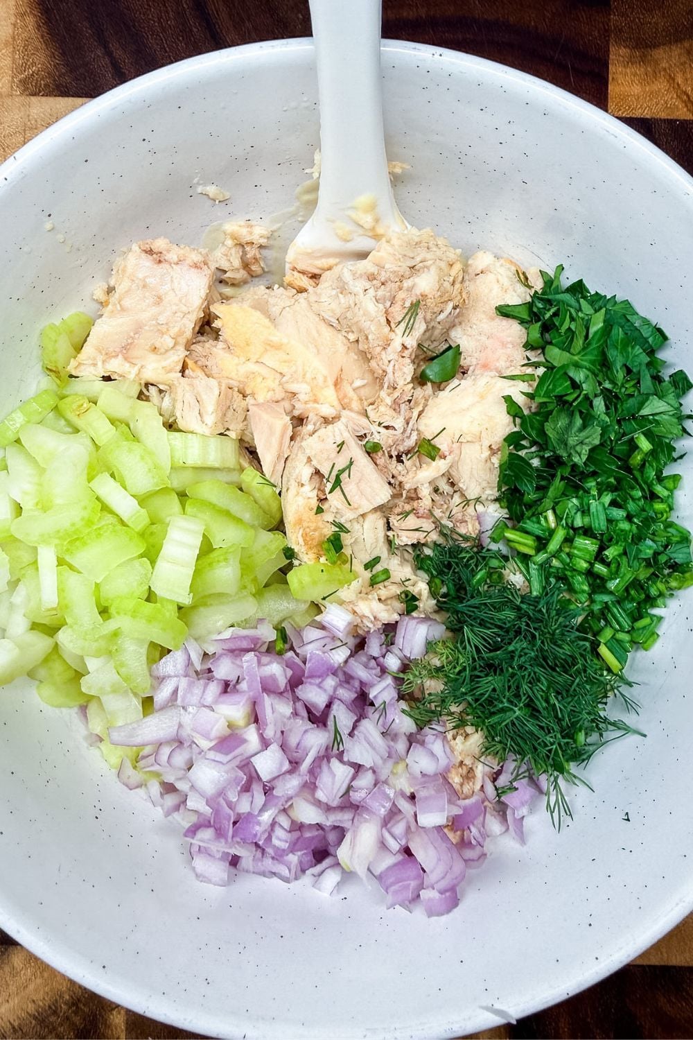 Tuna, celery, shallot, and fresh herbs prepared in a bowl for tuna salad