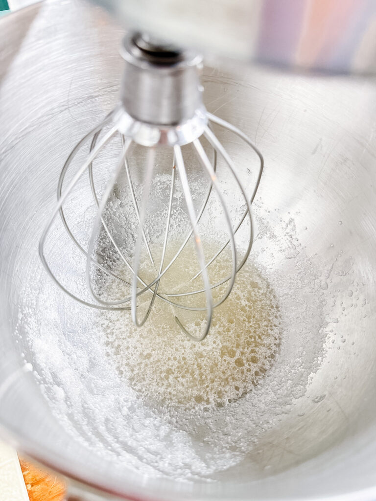 Bloomed gelatin mixture in a KitchenAid stand mixer bowl, bubbly and foamy with a whisk attachment