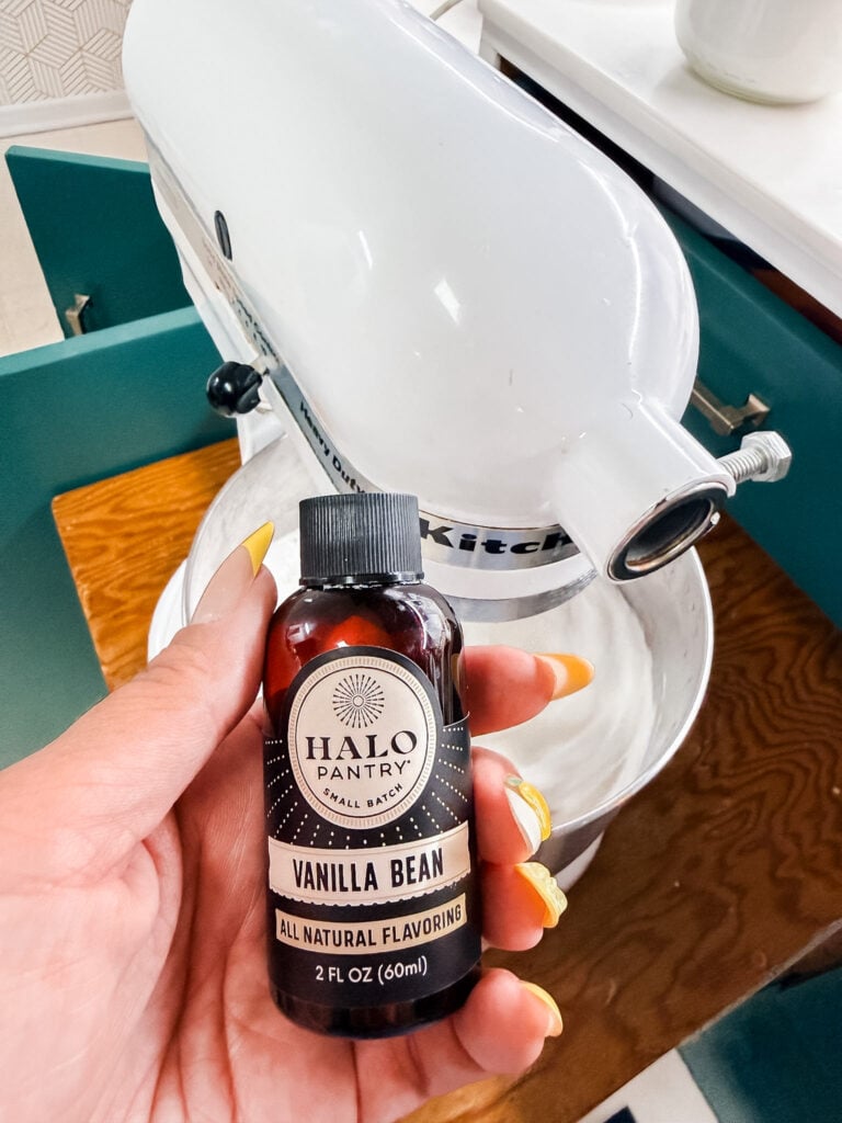 Hand holding a 2oz bottle of Halo Pantry Vanilla Bean All Natural Flavoring in front of a white KitchenAid mixer