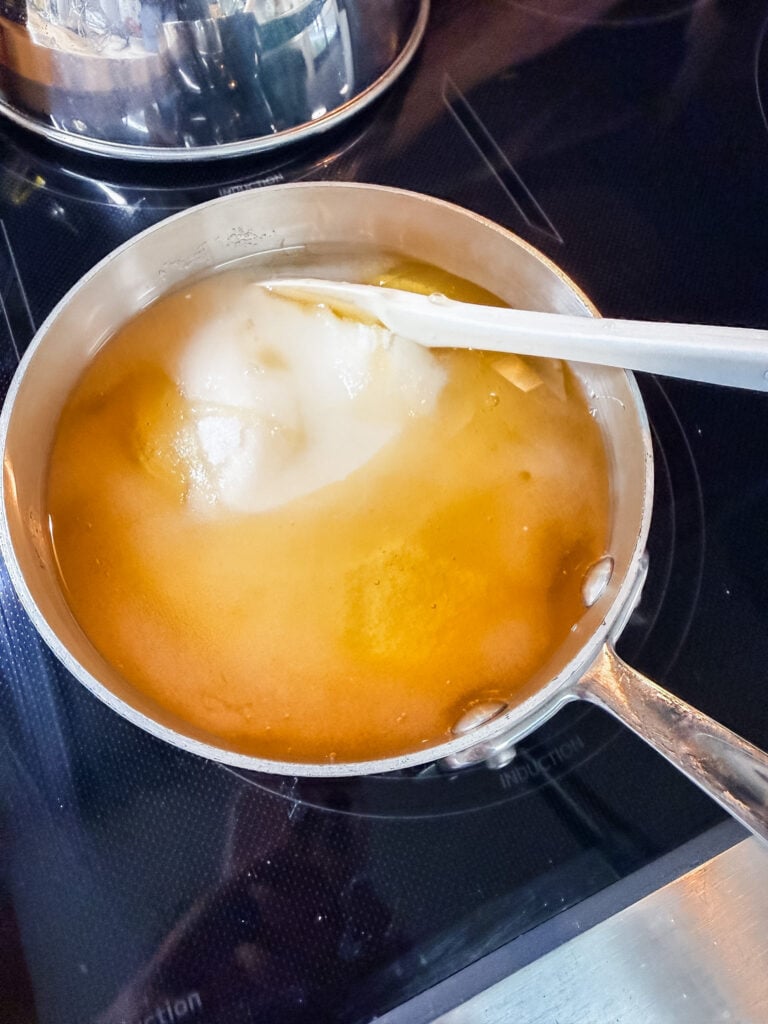 Honey and sugar syrup cooking in a saucepan on an induction stovetop, with a white spatula resting in the pan