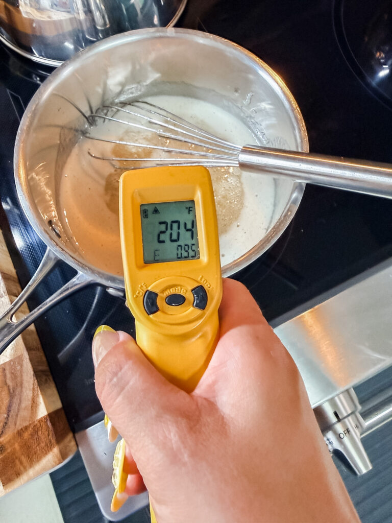 ThermoWorks infrared thermometer reading 204 degrees F held over a saucepan of sugar syrup with a whisk