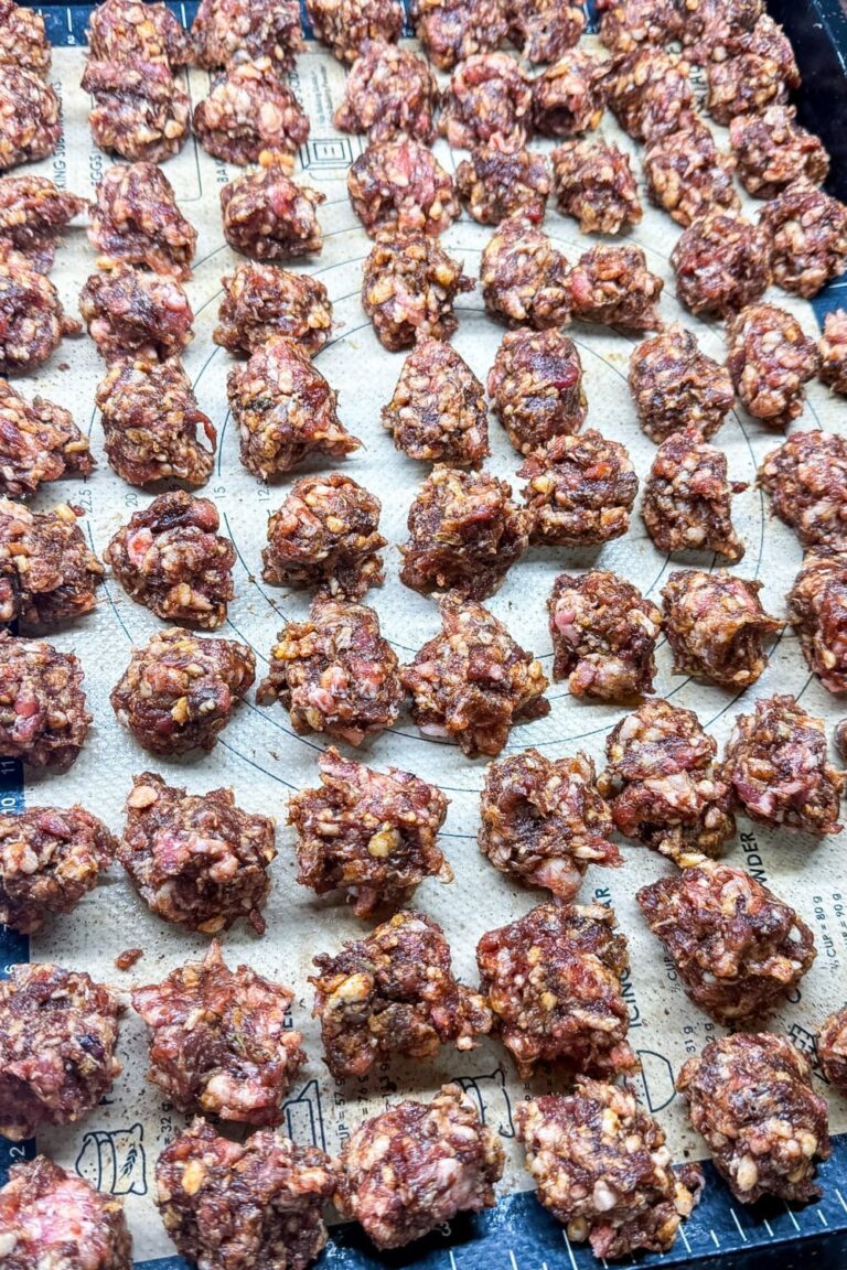 Raw homemade pizza sausage portions spread out on a parchment-lined sheet tray ready for freezing