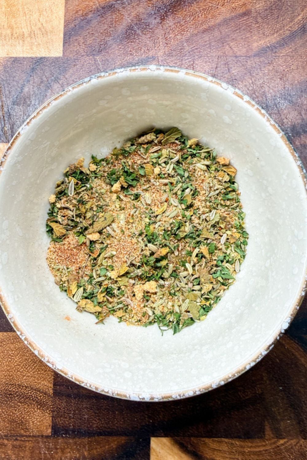 Finished homemade Italian sausage seasoning blend mixed together in a white bowl on a wood cutting board, ready to use or store.