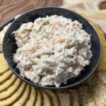 Creamy tuna salad served with assorted crackers on a wooden board