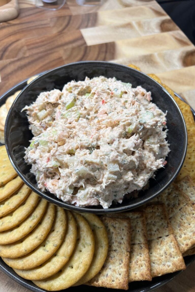 Creamy tuna salad served with assorted crackers on a wooden board