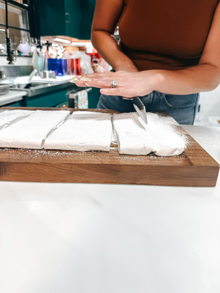 Cutting set marshmallow slab into large squares with a knife on a powdered sugar-dusted wooden cutting board
