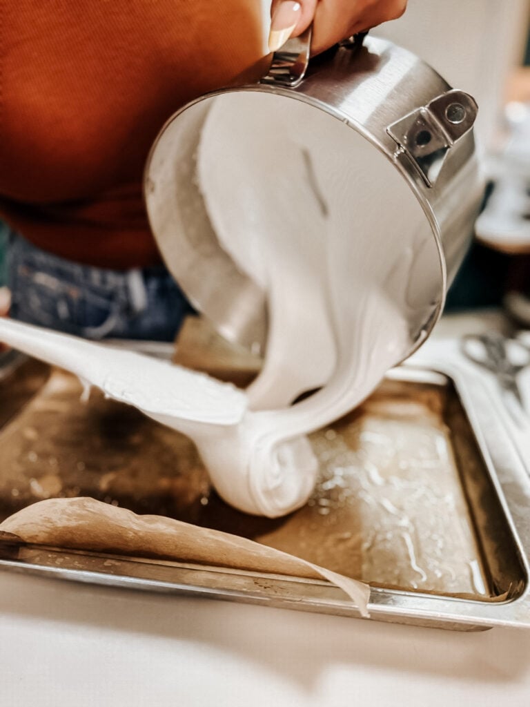 Close-up of thick white marshmallow mixture being scraped from a stand mixer bowl into a prepared baking pan