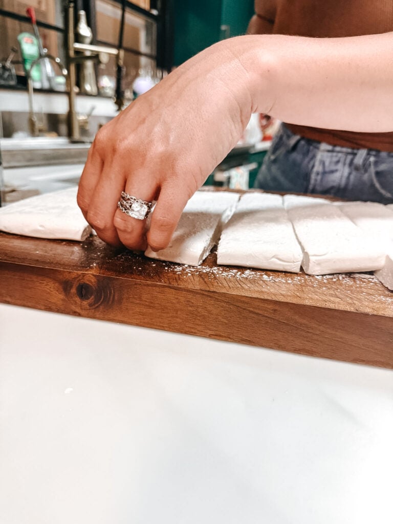 Homemade marshmallow slab being sliced into pieces on a wooden board, showing thick springy texture