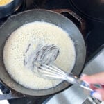 Flour just added to melted butter in a cast iron skillet, a spatula beginning to work the two together into a roux