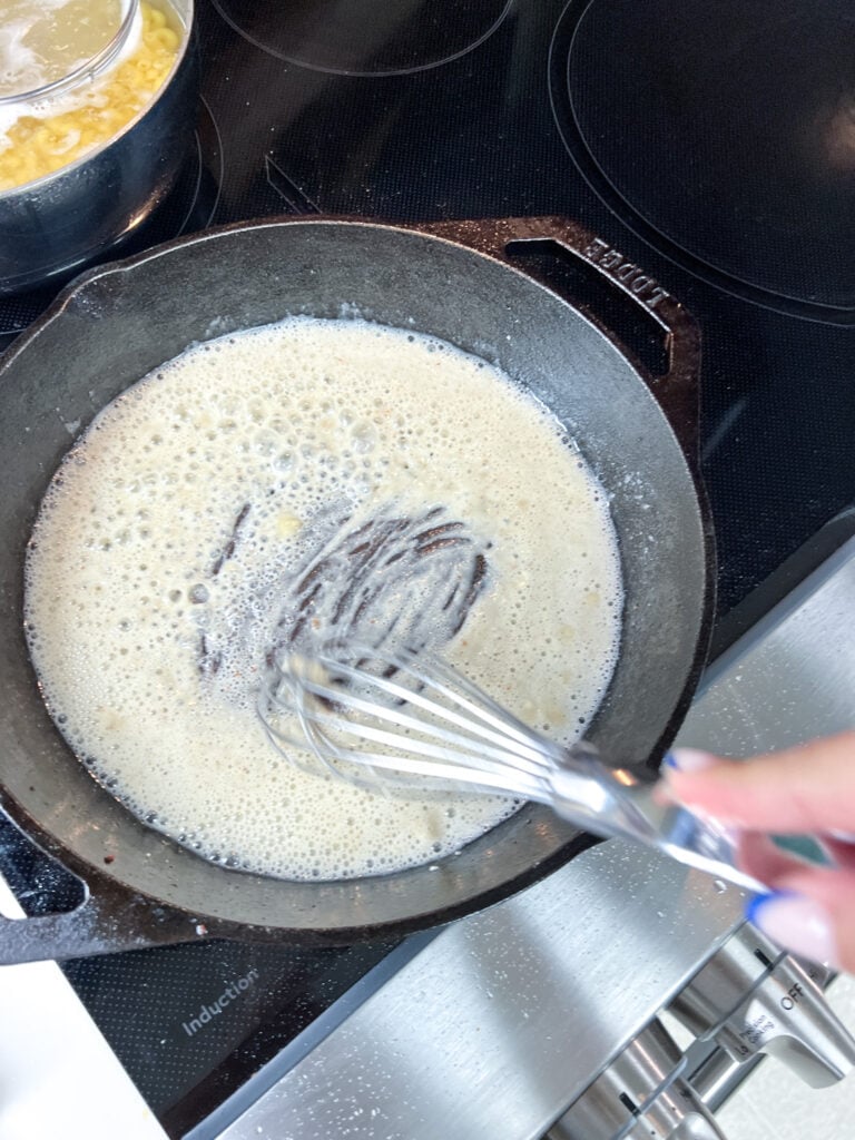 Flour just added to melted butter in a cast iron skillet, a spatula beginning to work the two together into a roux