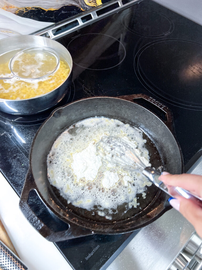 Early stage roux in a Lodge cast iron pan being whisked, butter and flour just beginning to combine on an induction stovetop
