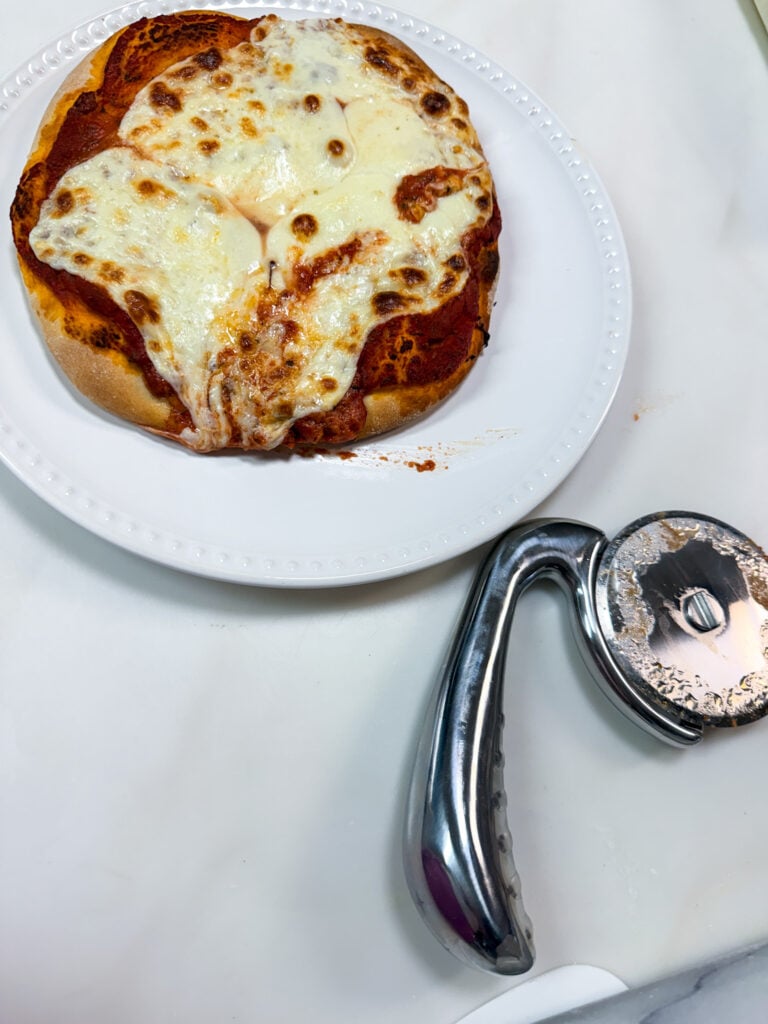 Freshly baked pizza with red sauce and melted mozzarella on a white plate with a pizza cutter