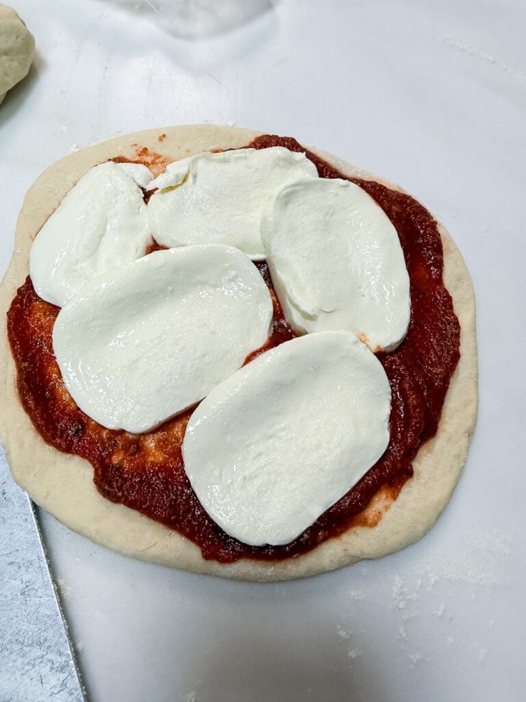 Unbaked pizza with red sauce and fresh mozzarella slices on homemade dough