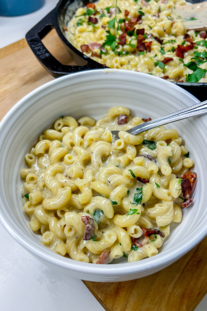 Smoked Gouda and Bacon Mac and Cheese in a dark skillet topped with crispy bacon crumbles and fresh chopped parsley