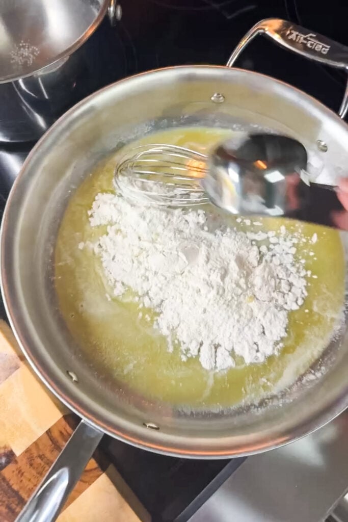 Flour being added to melted butter in a stainless steel pan — the first step of making a roux for mac and cheese