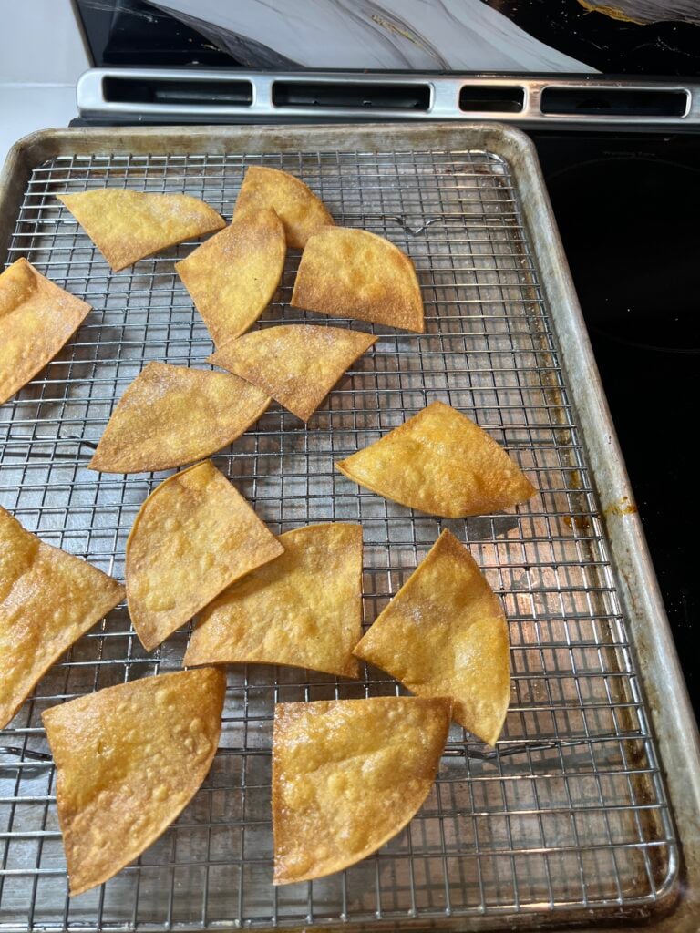 Freshly fried tortilla chips draining on a wire rack, still steaming