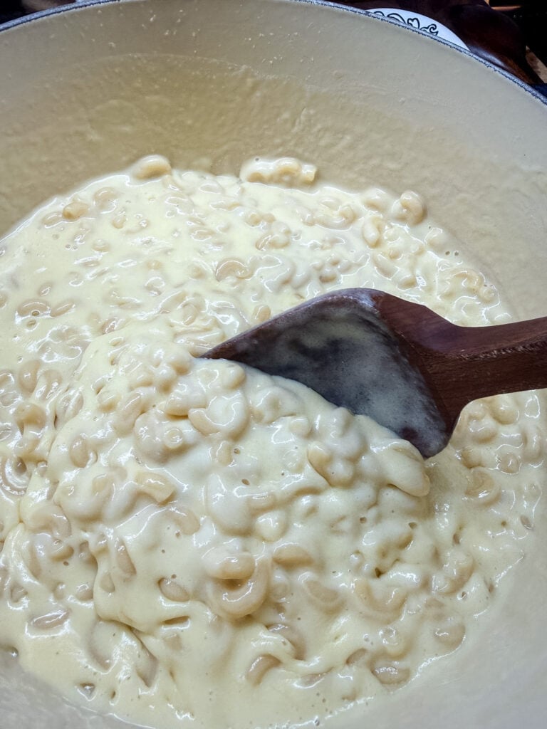 Finished creamy mac and cheese lifted on a wooden spoon, showing silky sauce coating the noodles