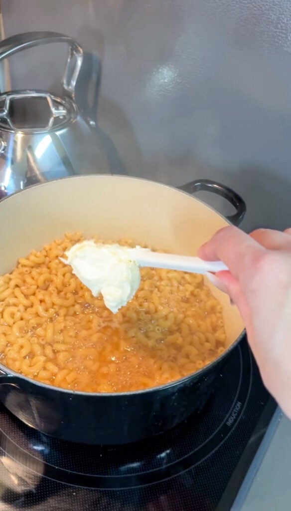 Elbow pasta stirring into broth as it cooks and absorbs liquid in a black Dutch oven