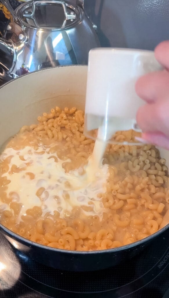 Heavy cream being poured into pasta and broth mixture in the pot