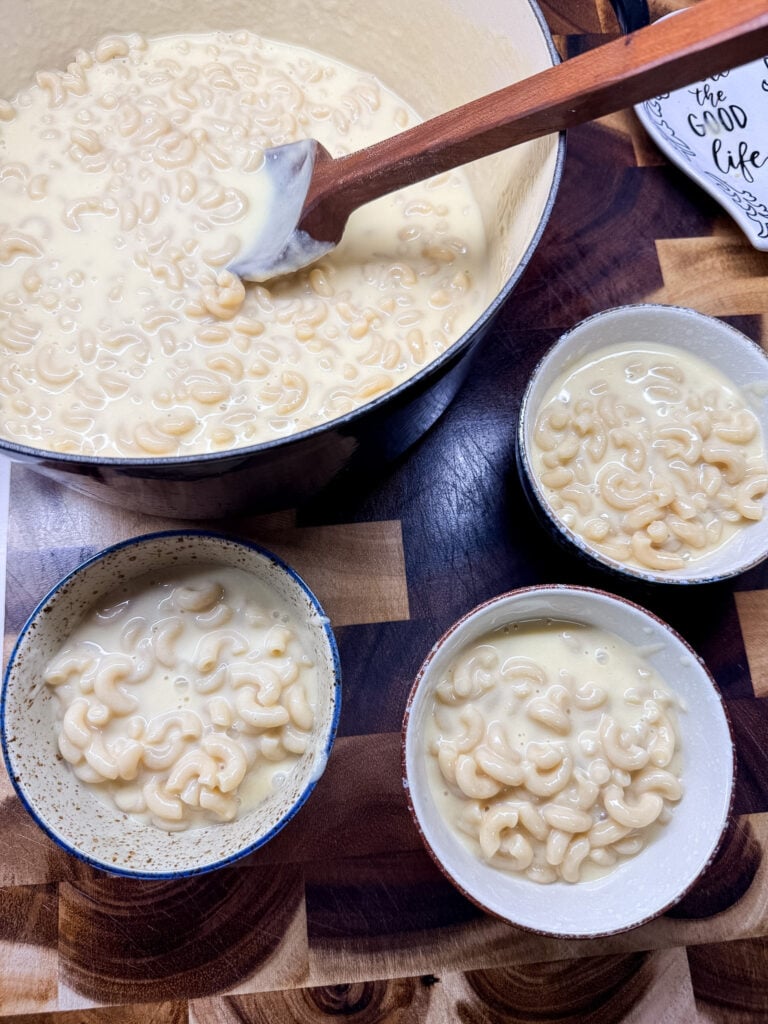 Three bowls of finished mac and cheese arranged on a checkered cloth with kitchen items in background