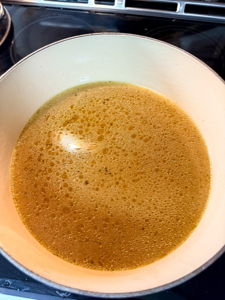 Finished golden-amber chicken broth filling a cream-colored Dutch oven, showing the clear, translucent liquid with rich warm color